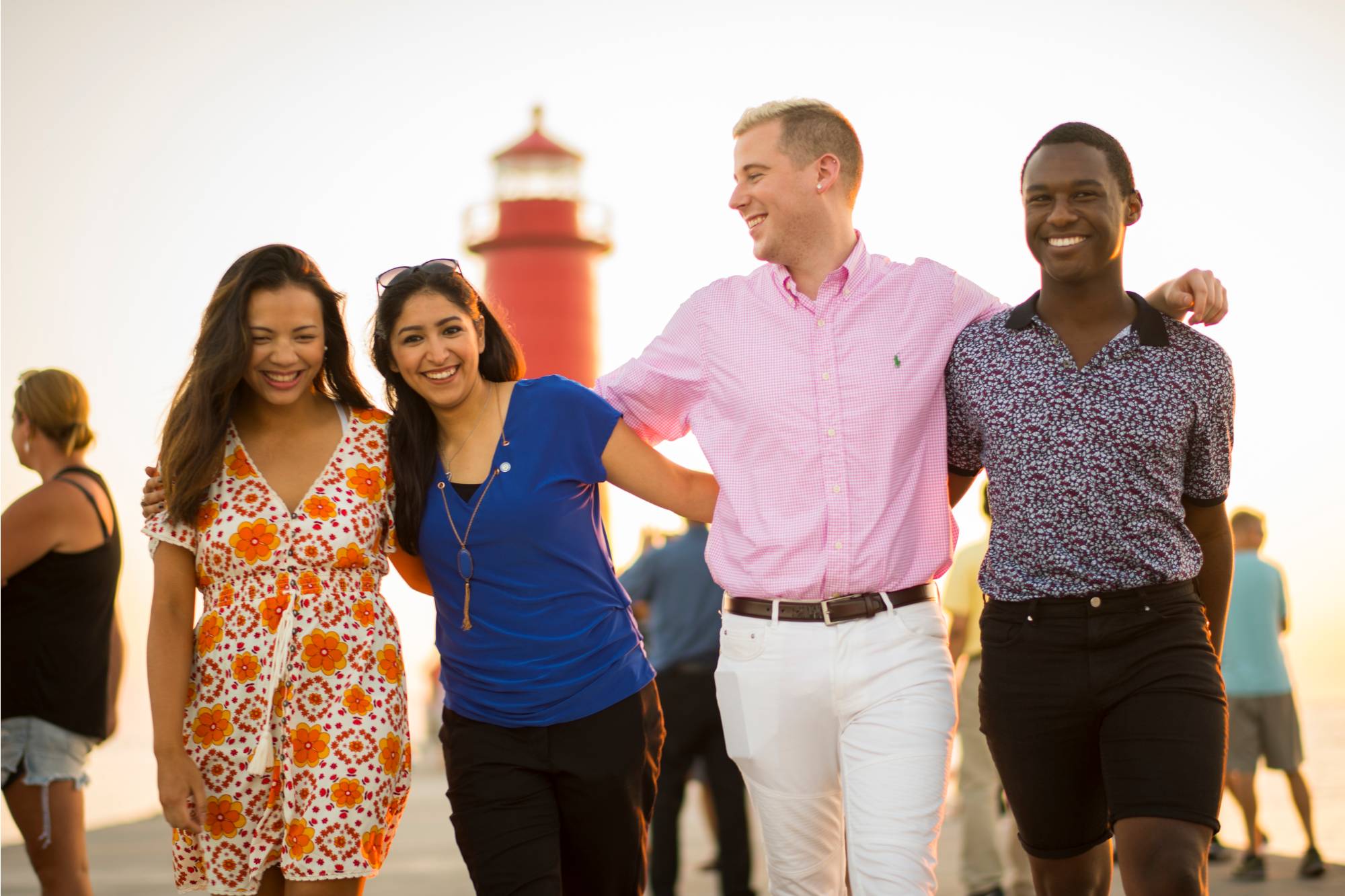 Four students walk closely with their arms around each other's shoulder on the pier at Grand Haven State Park.